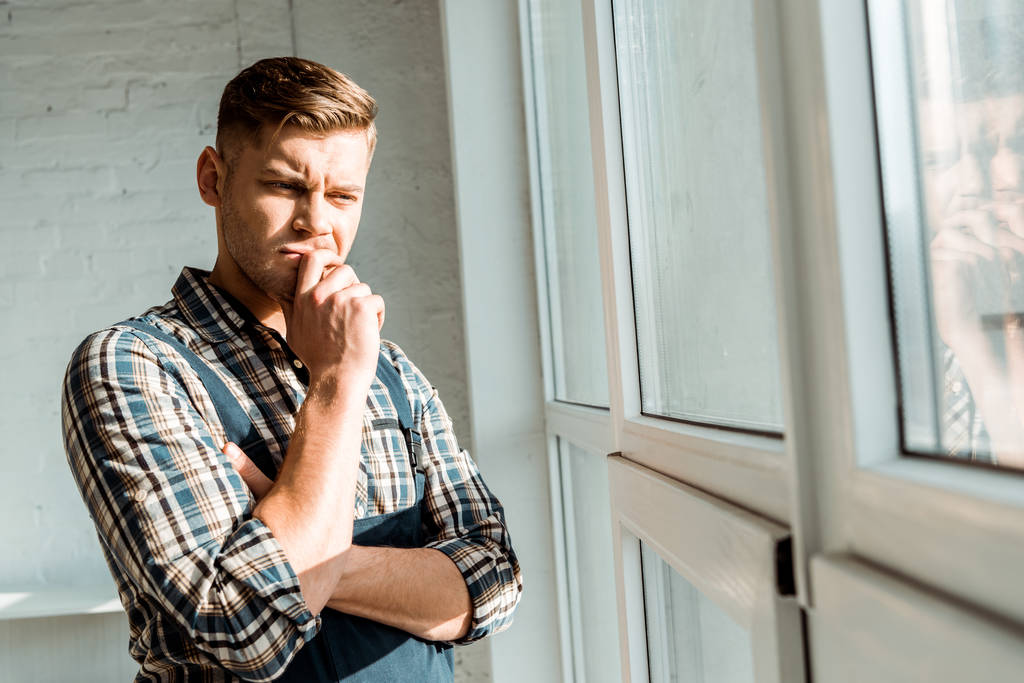 pensive installer touching face while thinking near windows