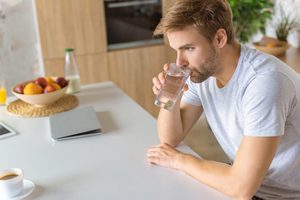  young man drinking water at kitchen table