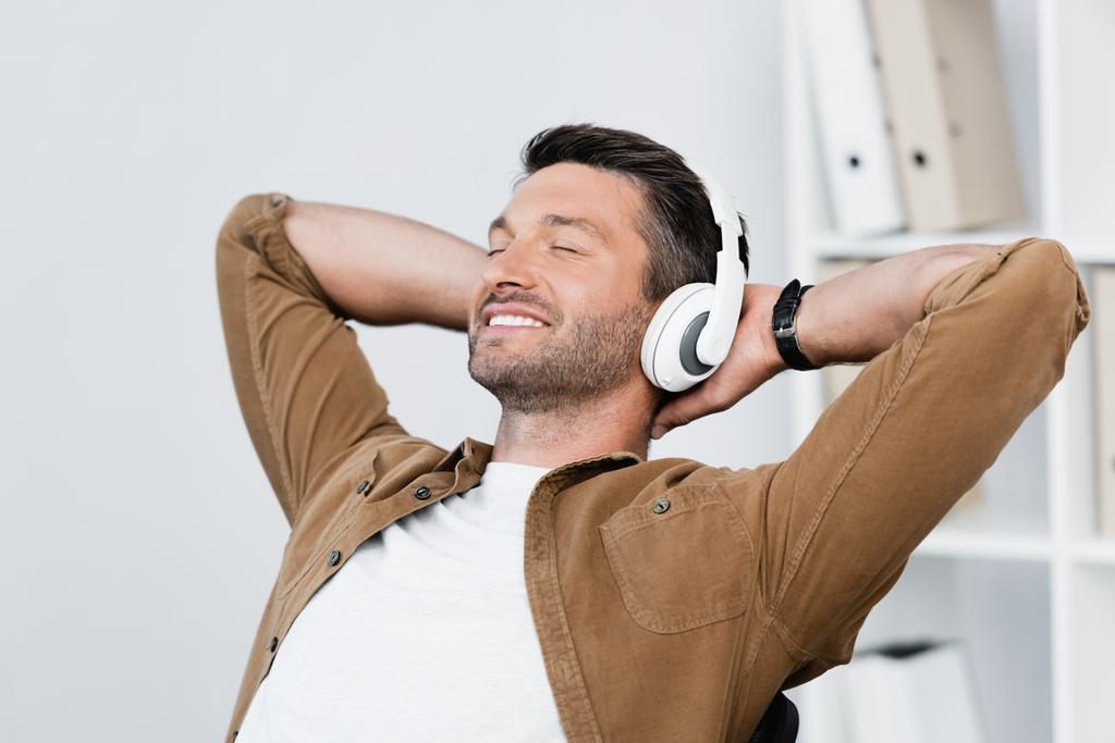 man in headphones relaxing while listening to music on blurred background 
