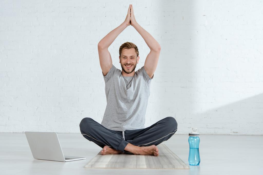 man looking at camera while practicing half lotus pose with raised prayer hands 