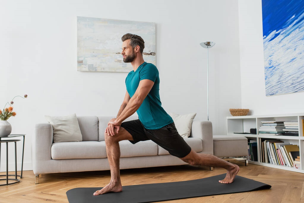 man practicing crescent lunge pose on yoga mat at home