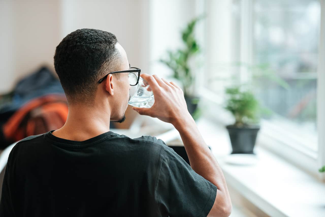 a young african man drinking water out of glass during coffee break at cafe 