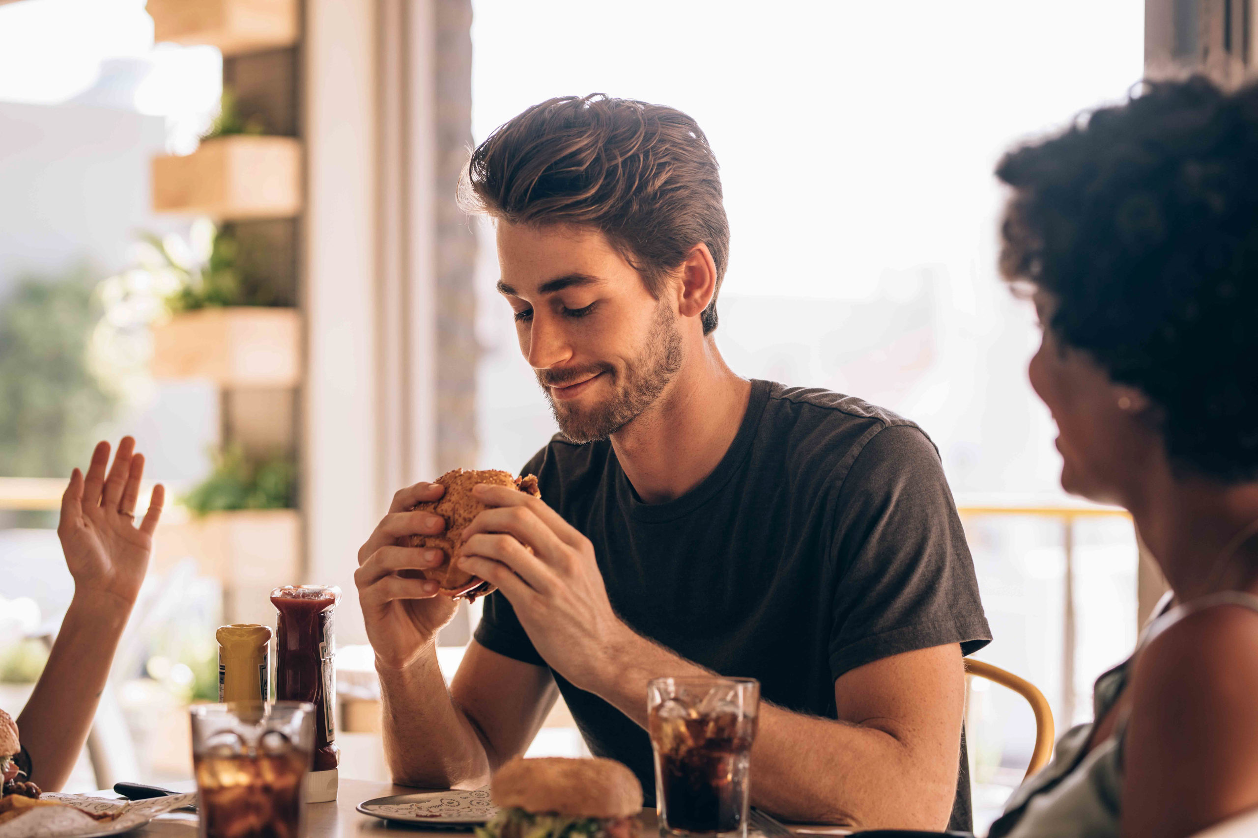 Young man eating burger while sitting with female friends at a restaurant