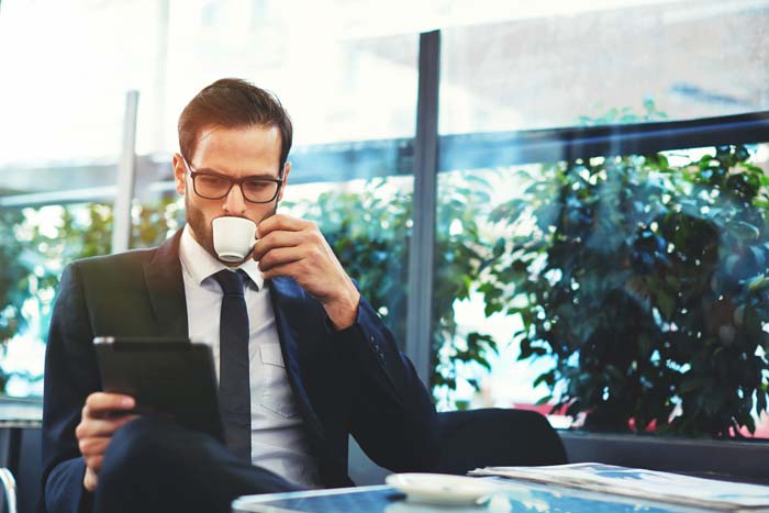 Portrait of handsome successful man drink coffee and look to the digital tablet screen sitting in coffee shop, business man having breakfast sitting on beautiful terrace with plants