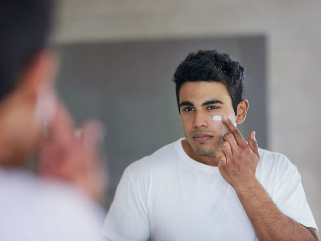 young man applying moisturizing cream 