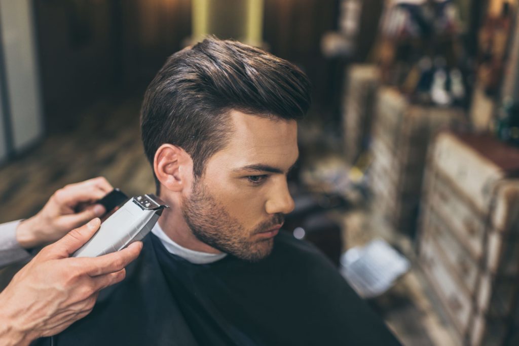 Barber Trimming Man's Beard With Trimmer In Men Hair Salon