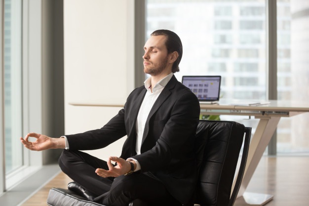 Man meditating in office coping with stress business executive doing yoga at desk in a modern office 