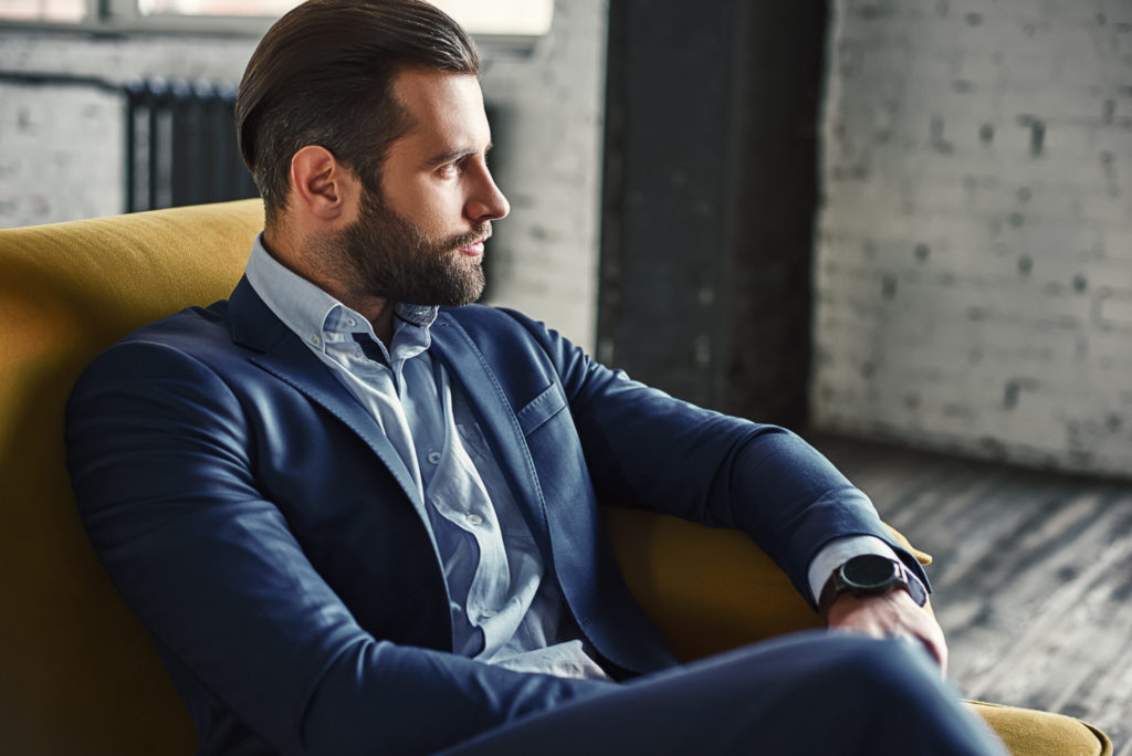 Young and charming businessman is thinking about business while sitting on the sofa in his modern office