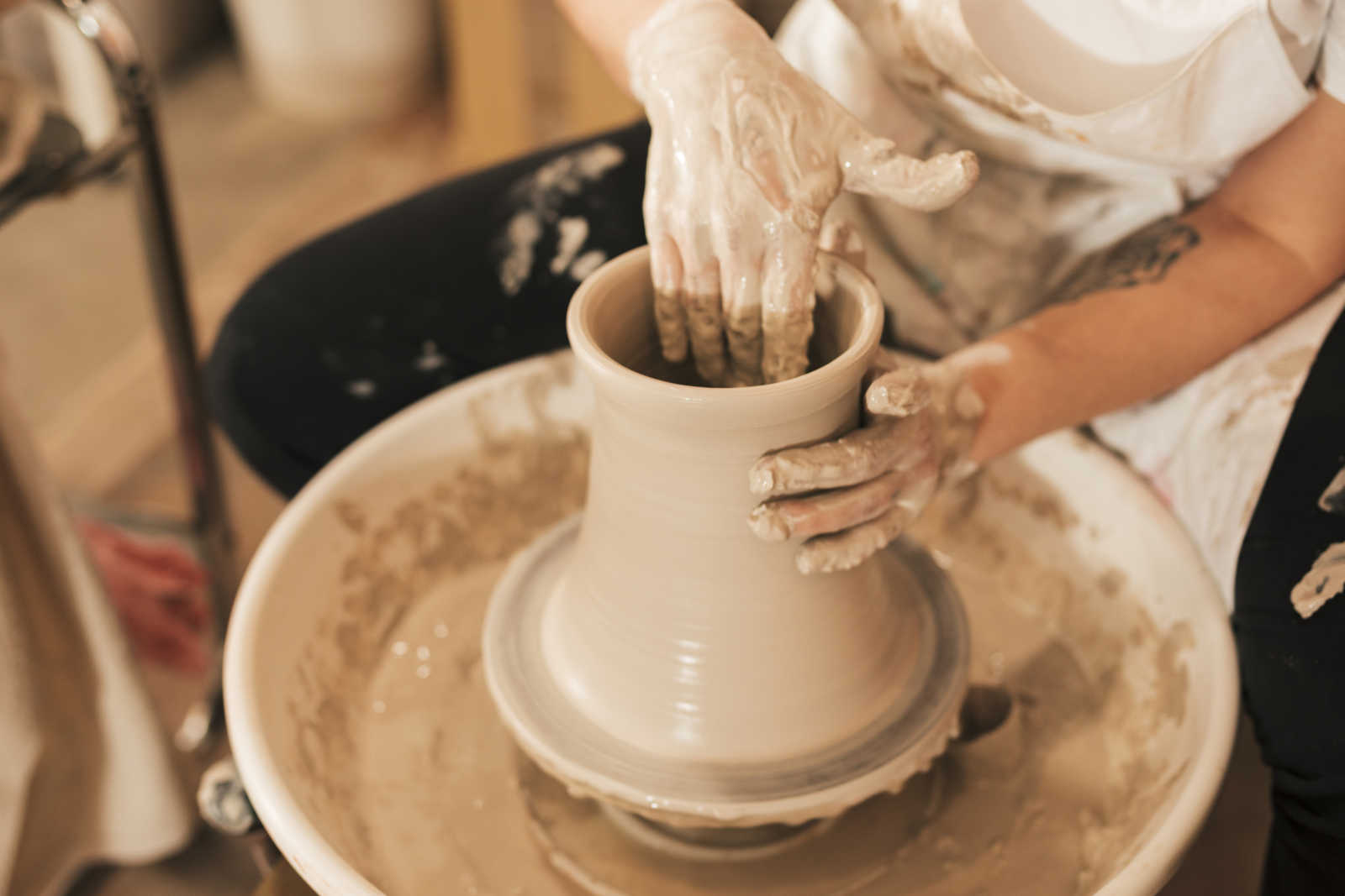 Female potter's hand making ceramic pot with clay on pottery wheel 