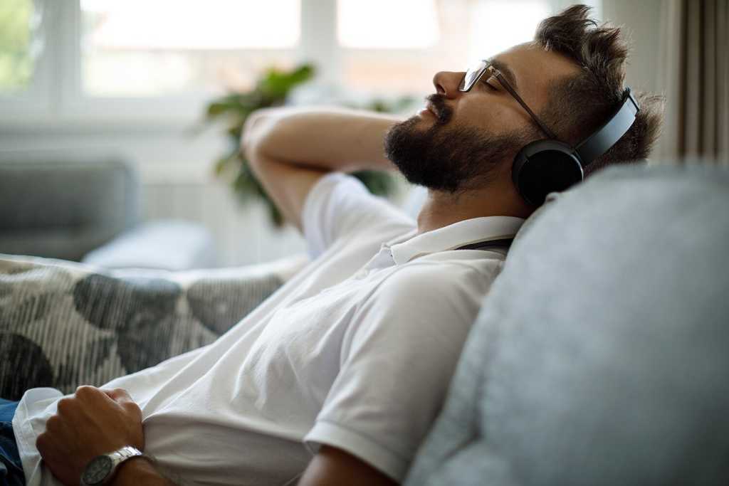 Young smiling man with bluetooth headphones relaxing on sofa