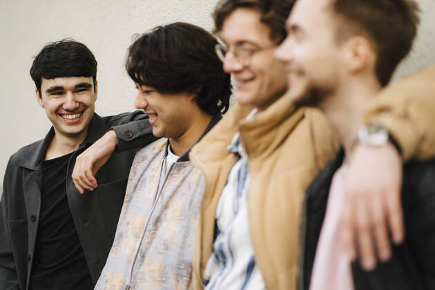 Smiling man looking at male friends standing with arms around 