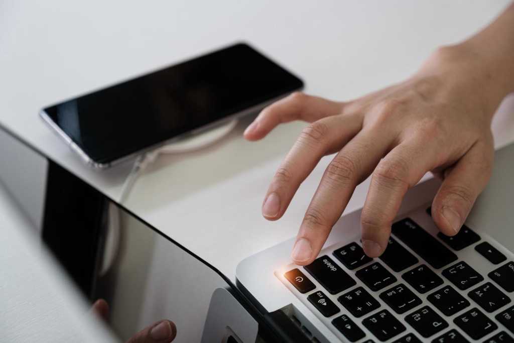  Man pressing the power button on a laptop computer to turn off smartphone, social media disconnect 