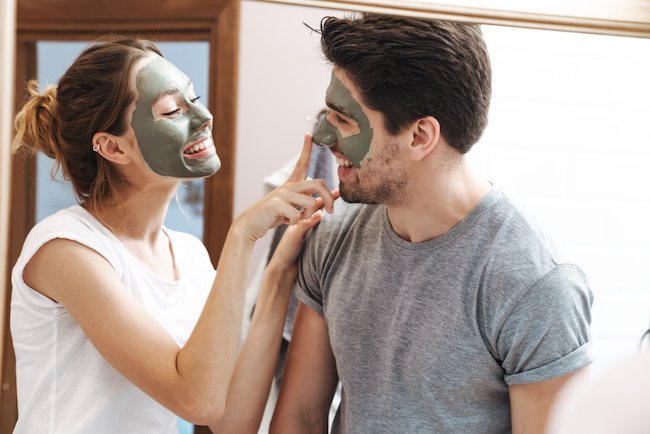  couple man and woman smiling while standing in bathroom with face mask