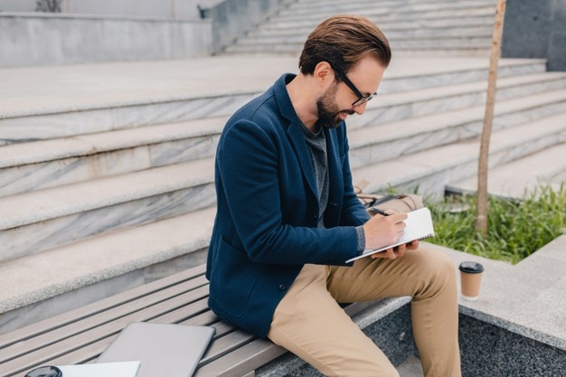 Handsome smiling bearded man working, writing in note book 