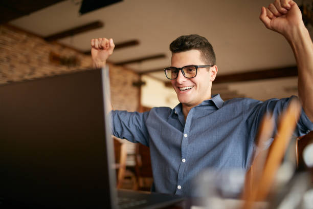 Handsome businessman with laptop having his arms with fists raised, celebrating success. Happy freelancer hipster in glasses finished work on project. Man won a lot of money in lottery prize. Business theme.