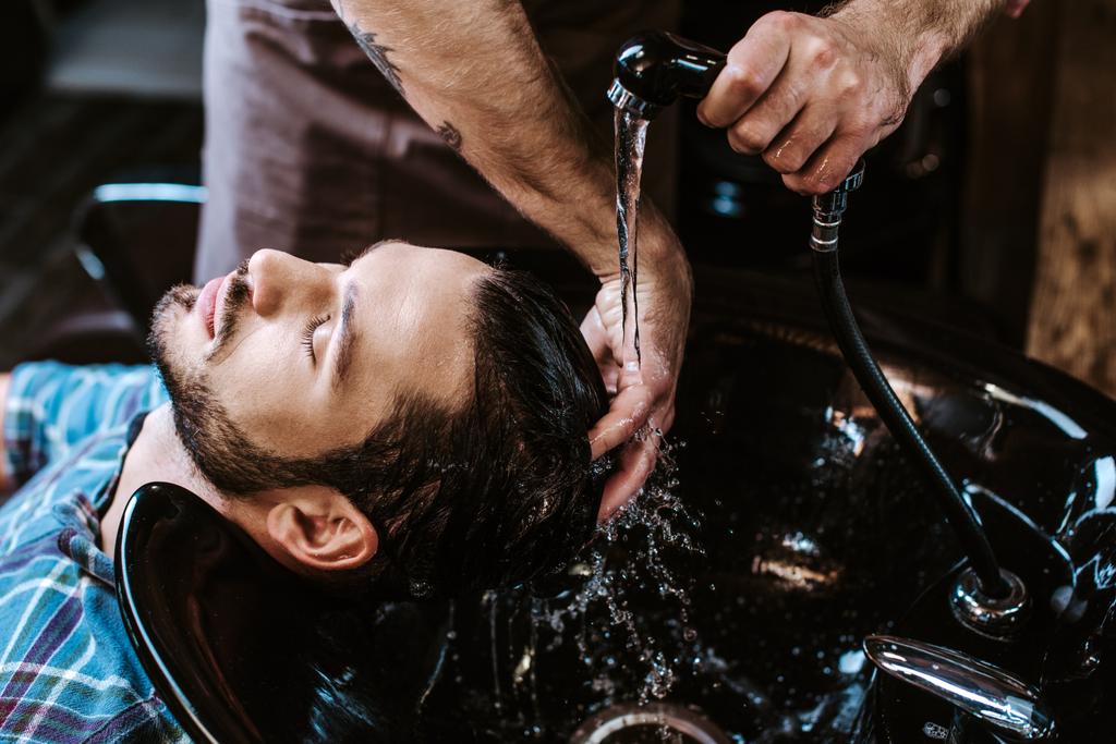 Tattooed Hairdresser Washing Hair Of Man 