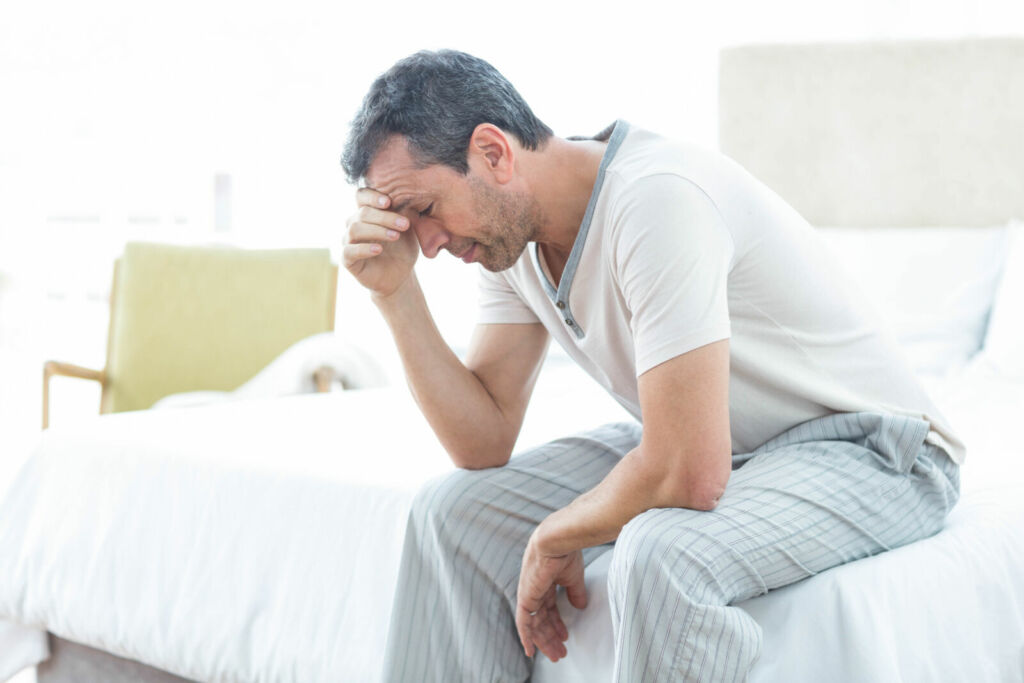 Worried man sitting on bed with hand on forehead