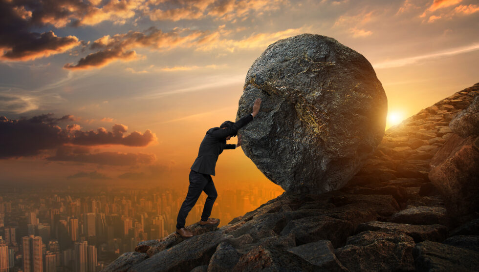 Business man pushing large stone up to hill 