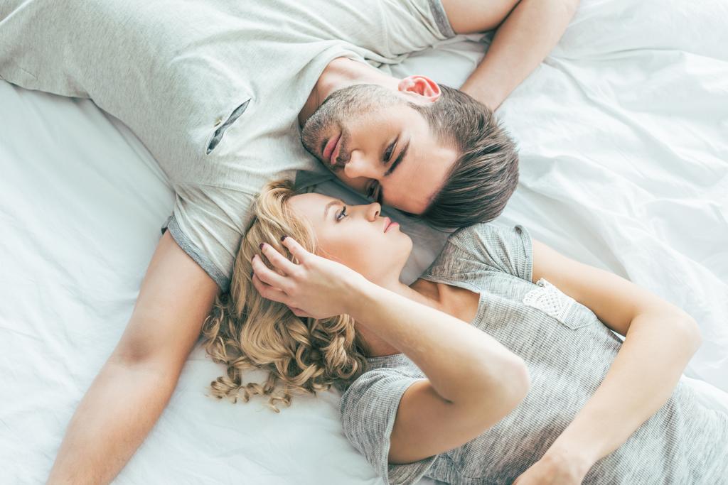 Beautiful young couple in love looking at each other while lying together on bed 