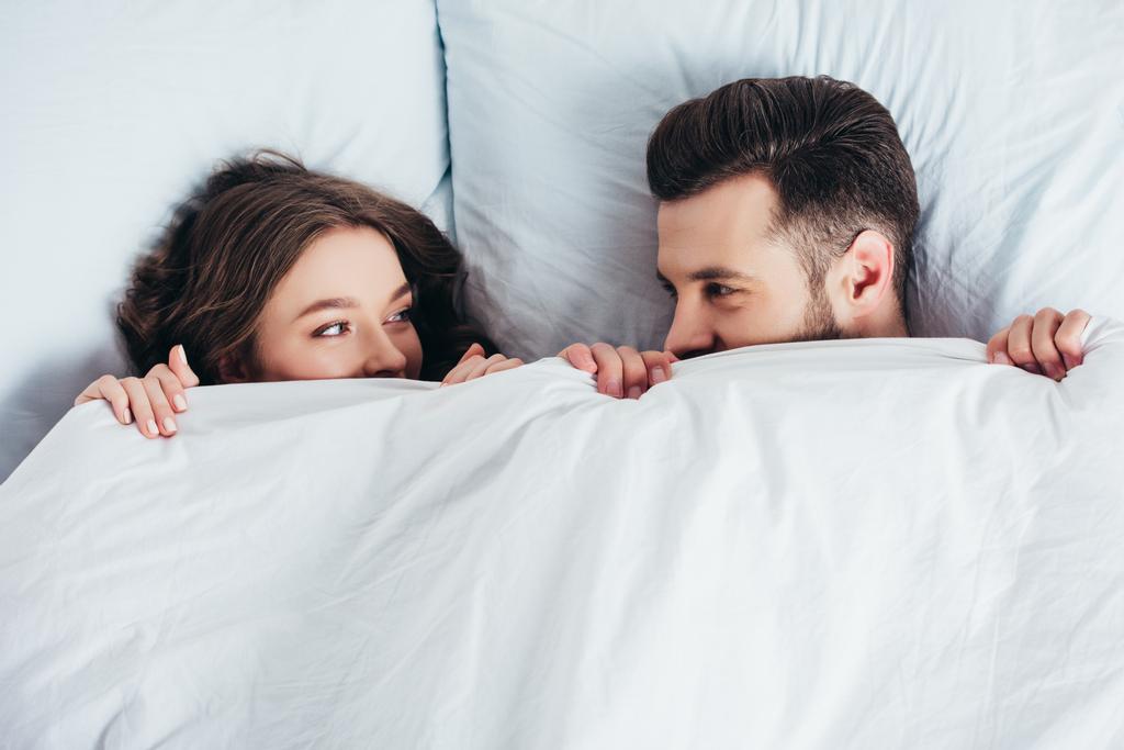 loving couple hiding under blanket in bed