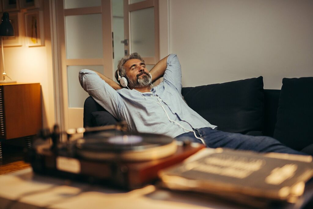 mid aged man listening music with headphones on record player, relaxed in sofa at his home