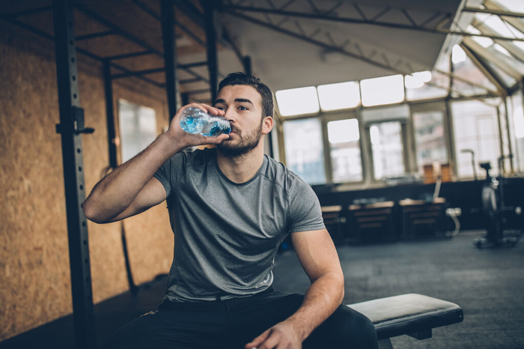 One man, sitting on bench, drinking water after training.